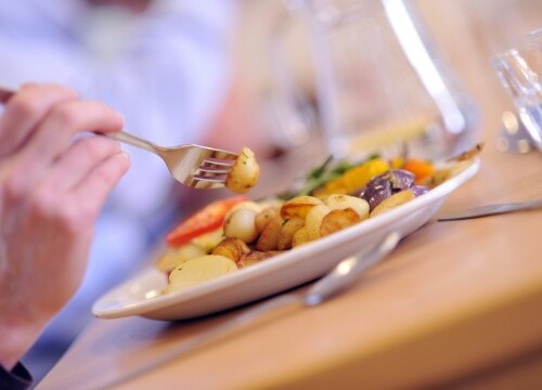 hand holding fork over plate of food