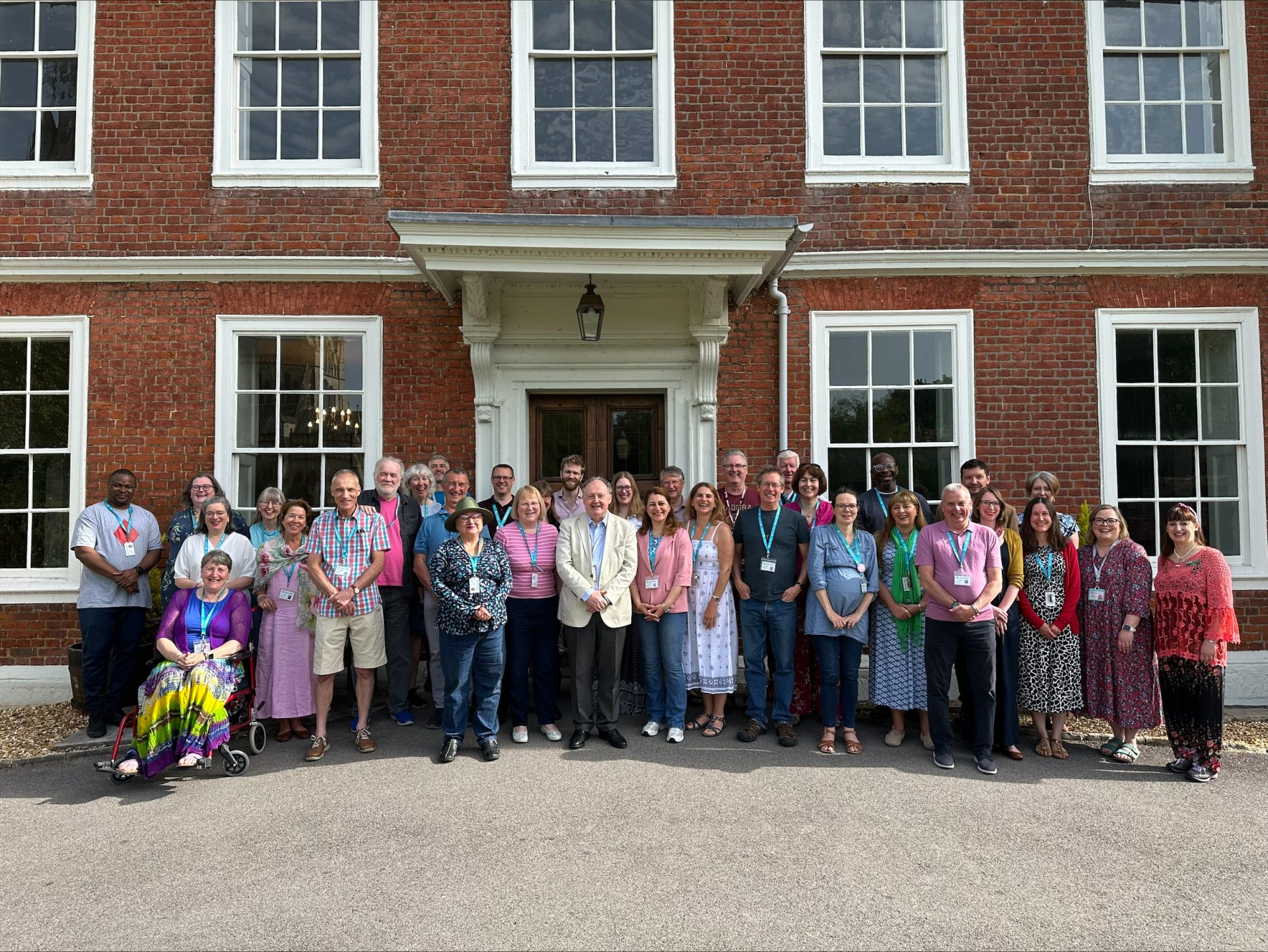 A group of smiling students and staff outside Sarum College on a sunny day
